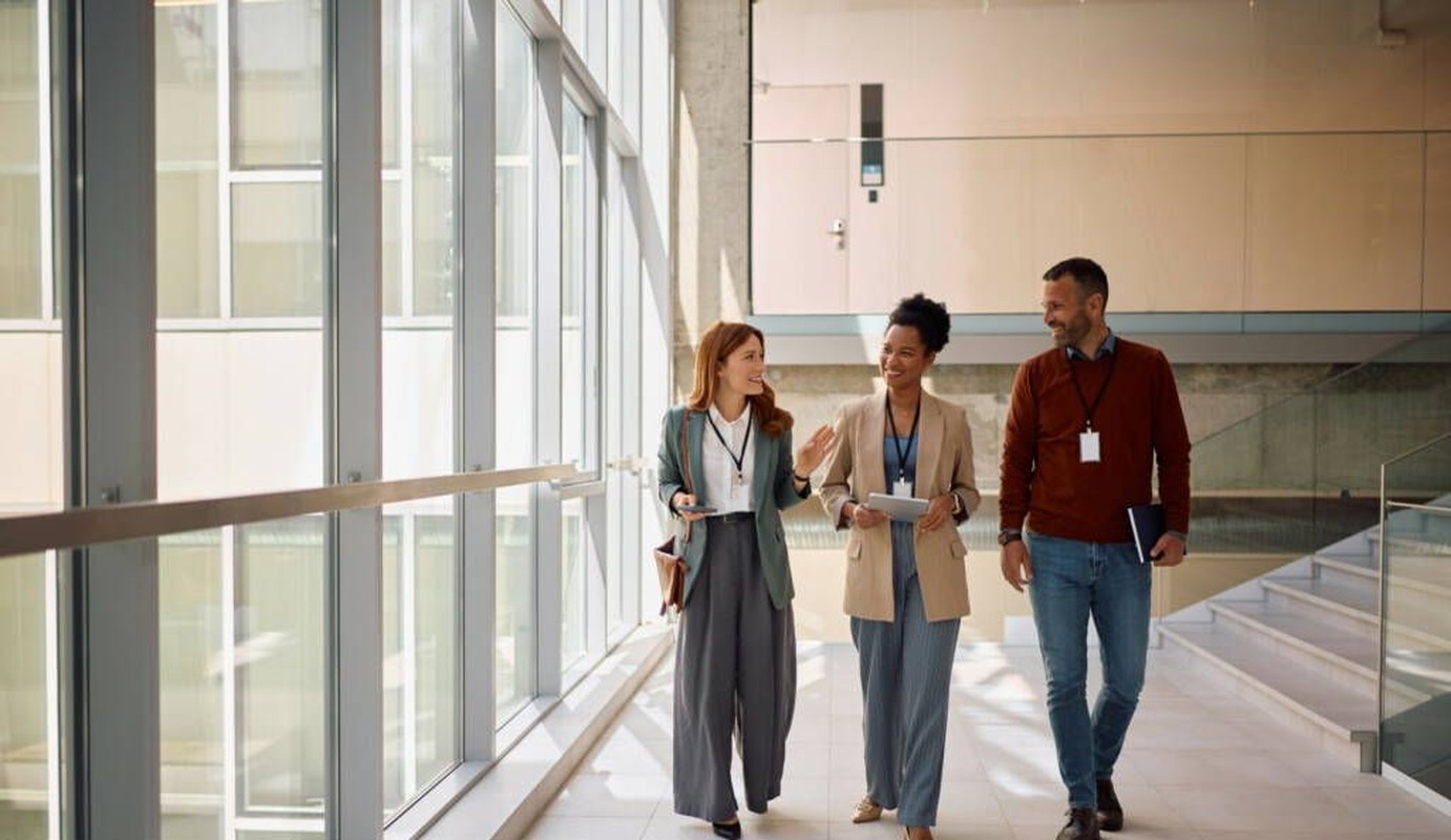 Tres profesionales conversando mientras caminan por un pasillo de oficina moderno
