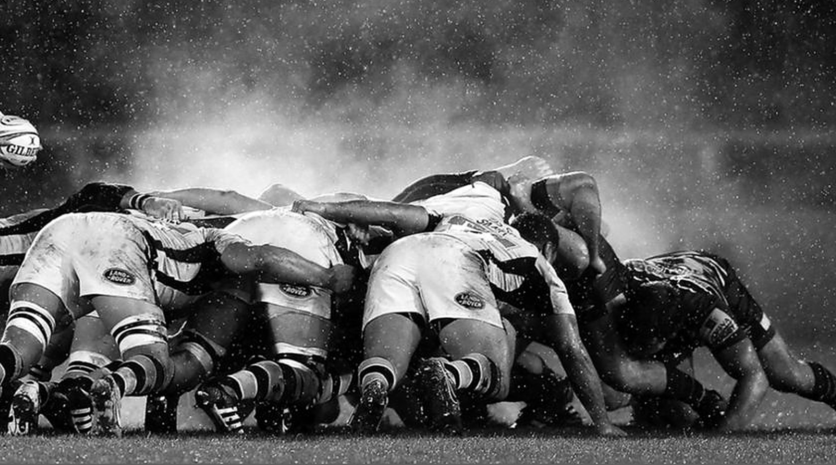 Primer plano de un scrum de rugby, jugadores trabados entre sí bajo la lluvia