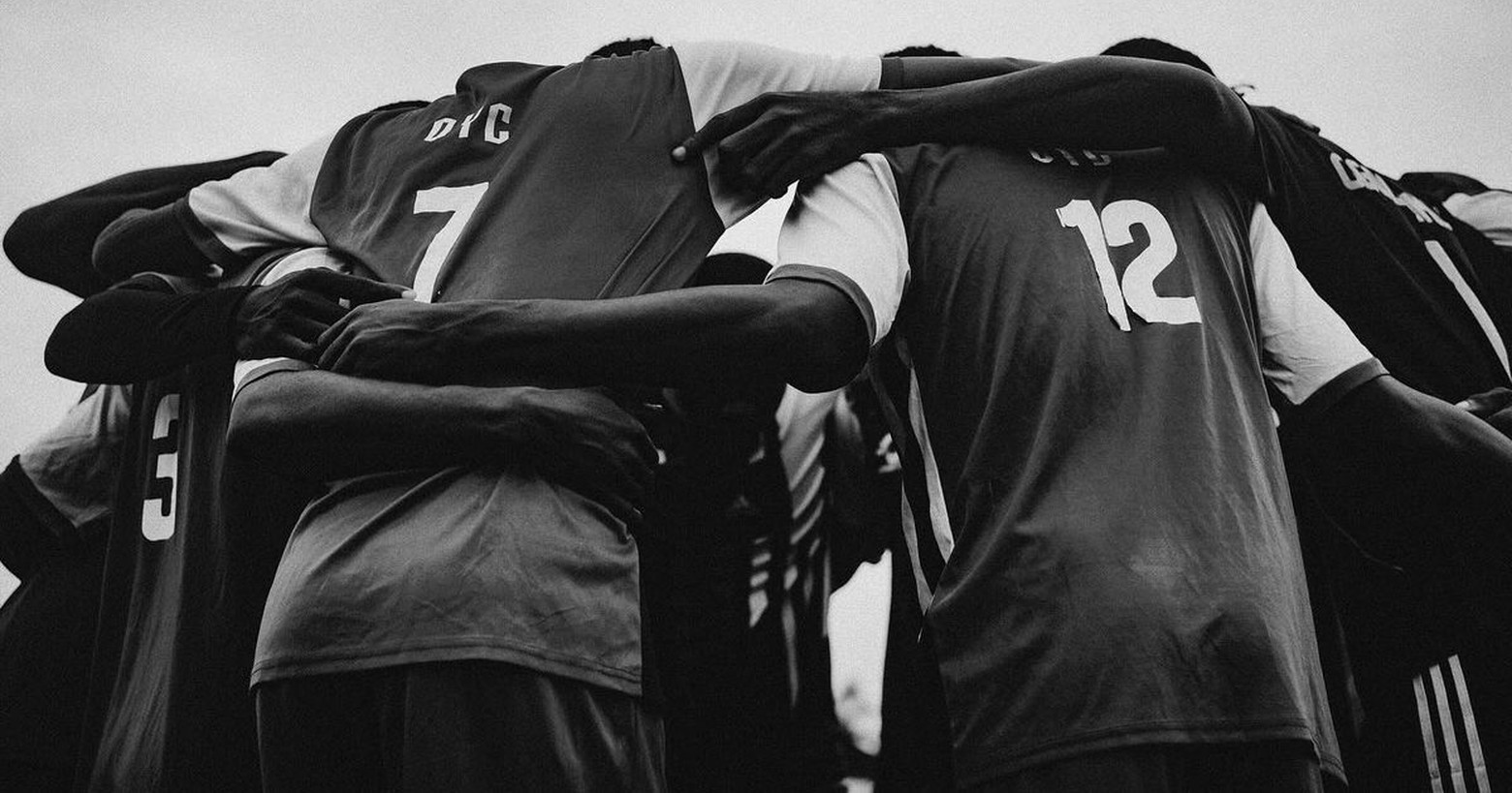 Equipo deportivo abrazado en huddle, fotografía en blanco y negro con números en las camisetas