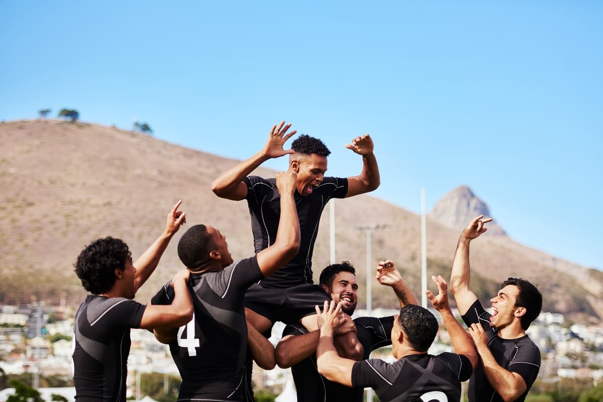 Equipo deportivo celebrando al aire libre, levantando a un compañero
