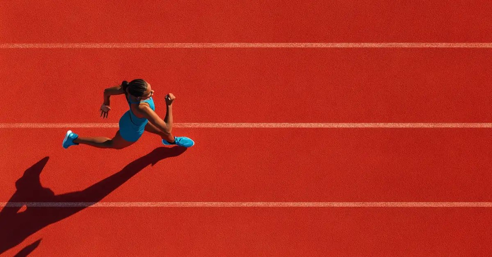 Vista aérea de una velocista en plena carrera sobre una pista de atletismo roja